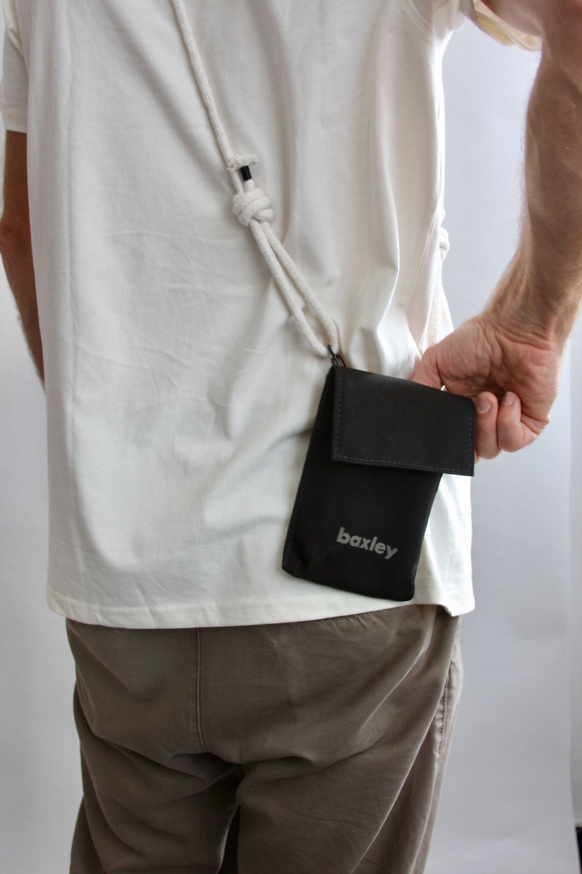 A male model is shown wearing Pip the pocket. The bag is black with a screenprinted logo and white rope strap.
