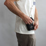 Pip the pocket worn cross-body on a male model. The bag is black, has a screen-printed logo, and a white rope strap. The model is opening the bag.