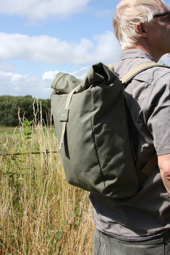Man wearing a Sage Green Baxley Rolltop backpack stands in a field.