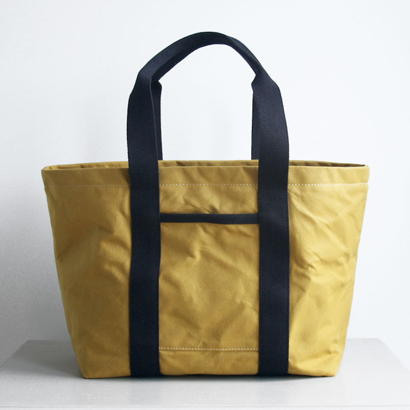 Front view of Hank the tote from Baxley. Shown in cumin with black webbing, with a front pocket visible.