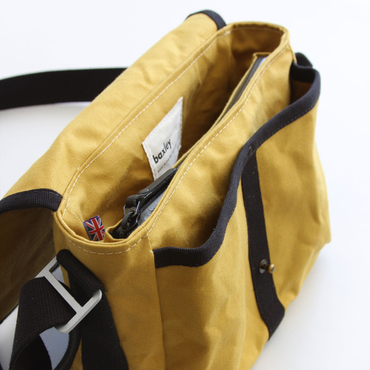 Interior view of Gertie the crossbody satchel from Baxley in cumin and black. A zippered pocket and two drop pockets are visible, as is a made-in-uk flag.