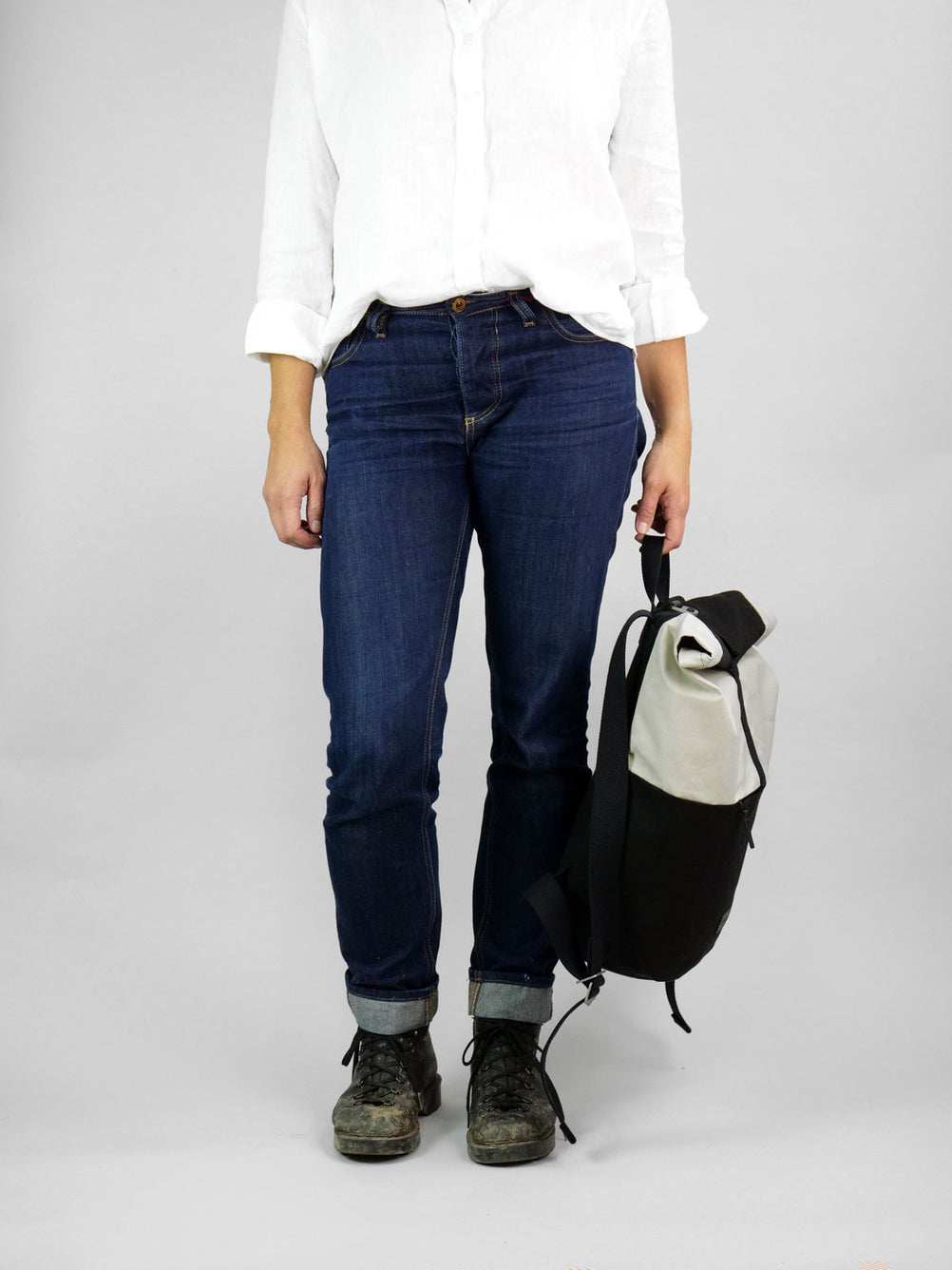 Informal woman easily holding Max the backpack. A rolltop backpack made of waxed canvas in chalk white and black, being held by a handle on top of the bag. 