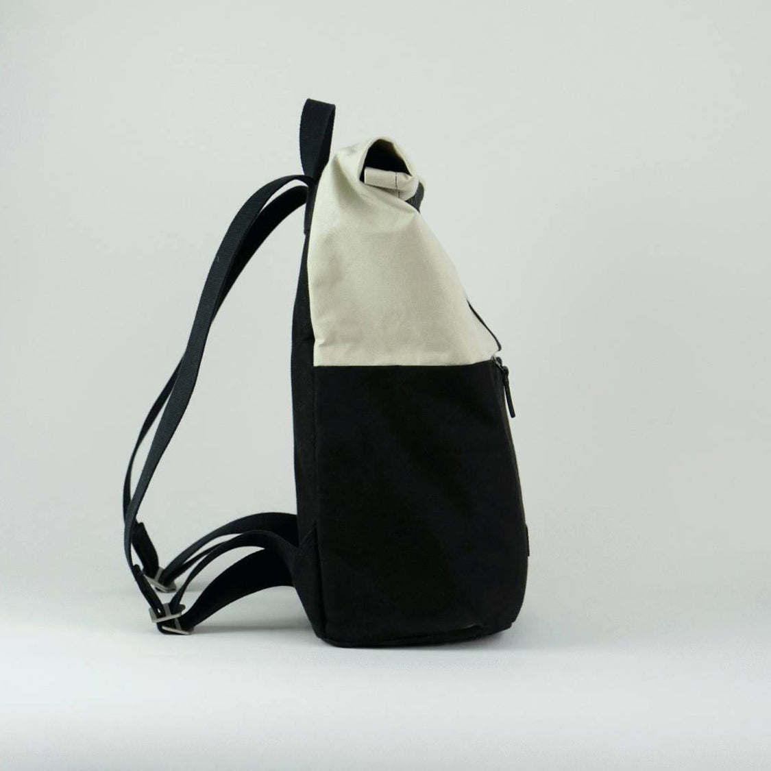 Side view of Max the backpack. A rolltop backpack made of waxed canvas in chalk white and black, with a side zipped pocket visible for storage of phone or keys.